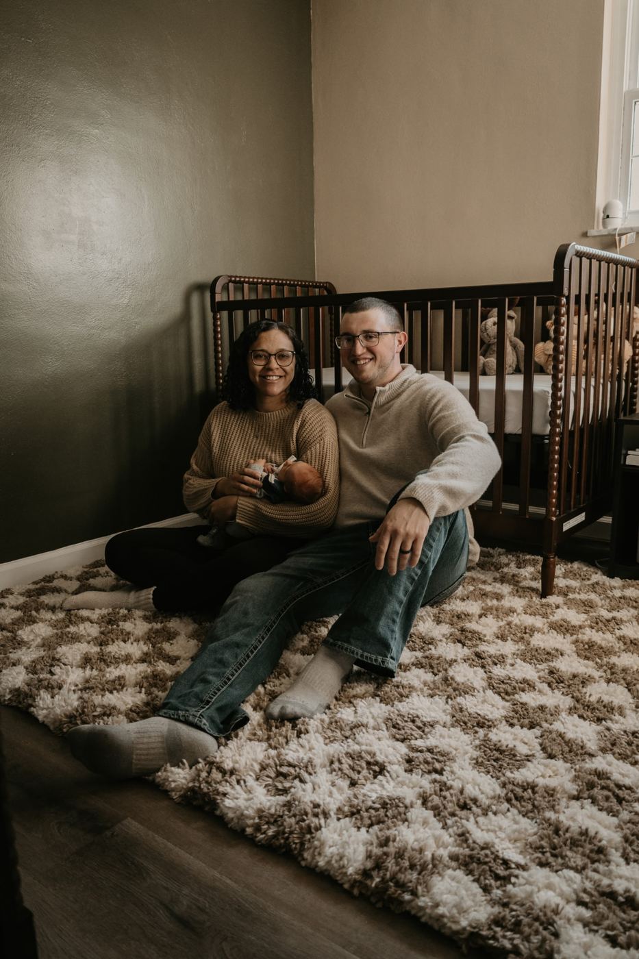 A'leigha and her husband sitting together with their baby boy in his nursery