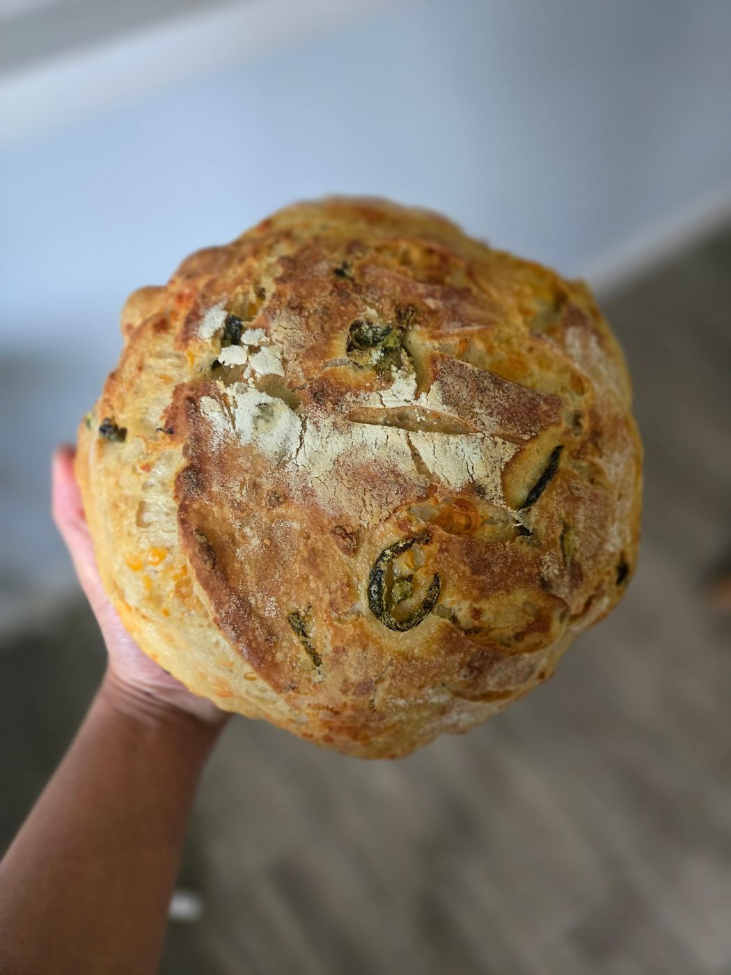 A round loaf of jalapeño cheddar sourdough bread with a scored, golden crust